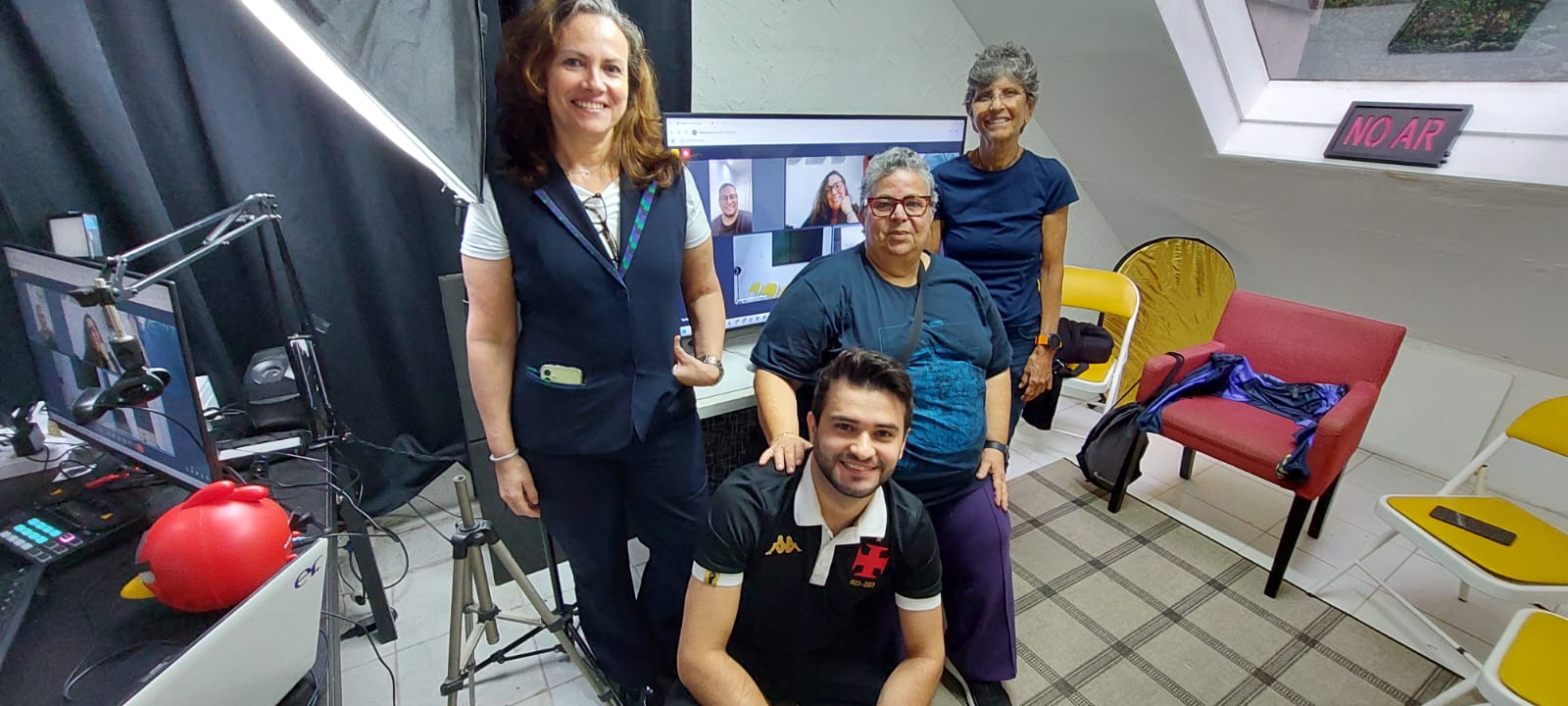 Turma reunida no estúdio da Escola de Rádio com placa NO AR acesa