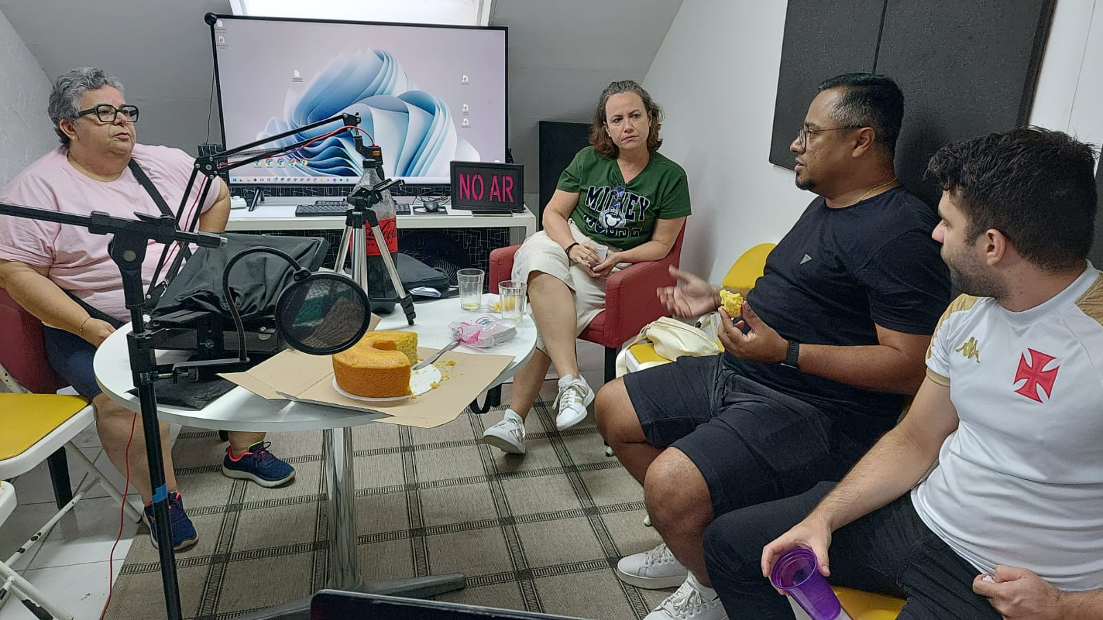 Turma comemorando aniversário com bolo no estúdio de podcast