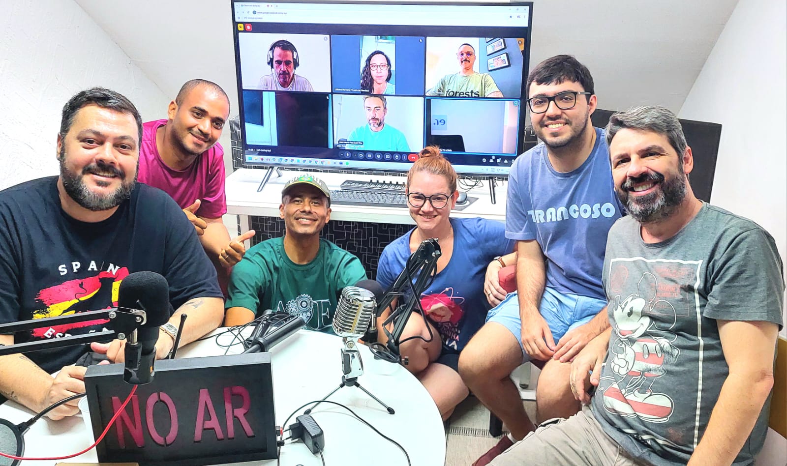 Turma de seis alunos com placa NO AR e colegas em chamada online na tela
